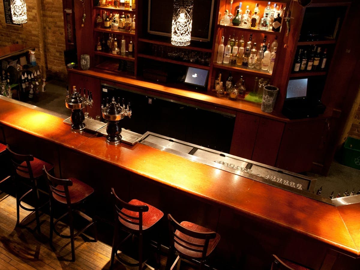 Empty bar with a polished wooden counter, two draft beer towers and backlit shelves