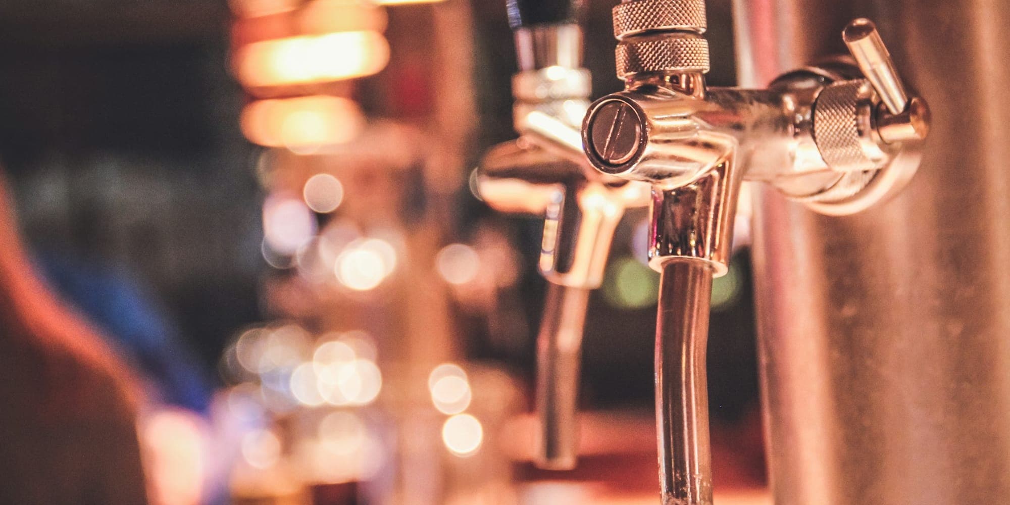 Close-up of a chrome draft beer faucet with a blurred bar behind it