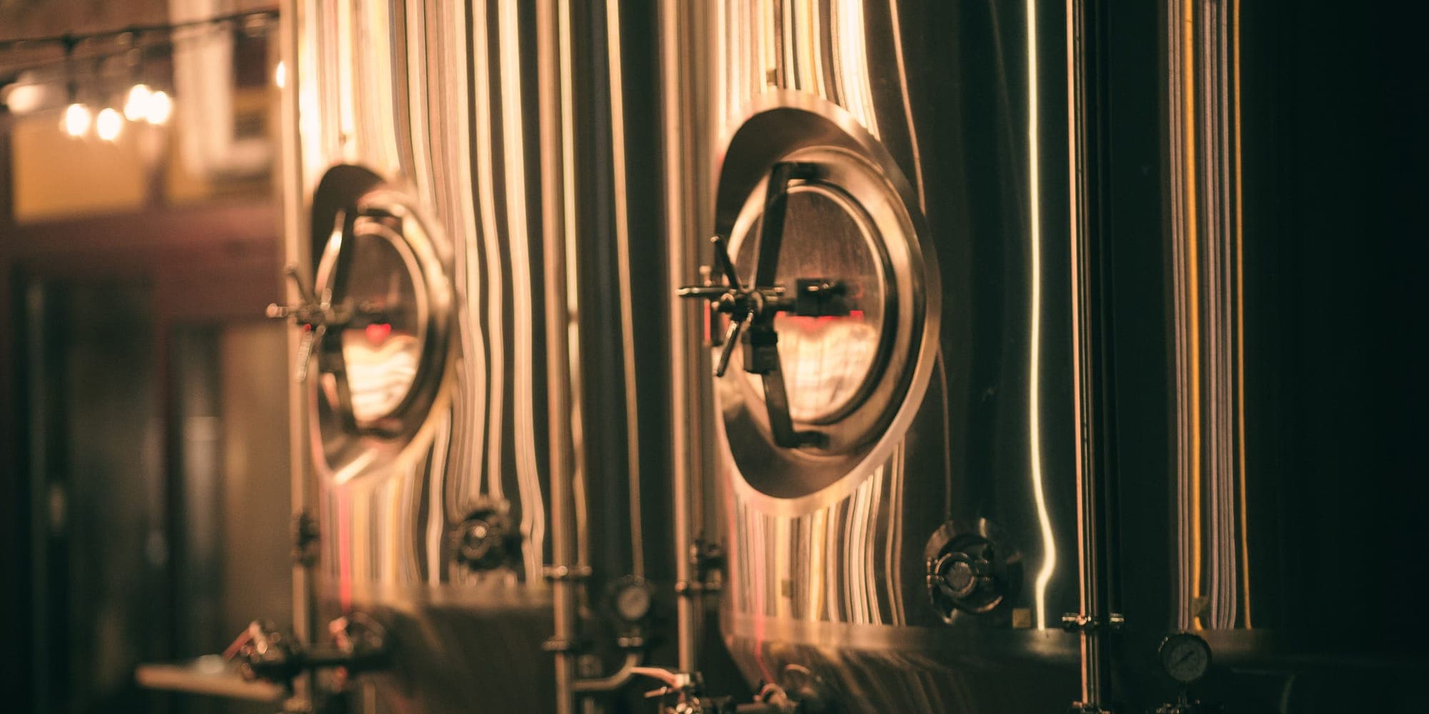 Stainless steel brewery tanks with round manway doors in warm light
